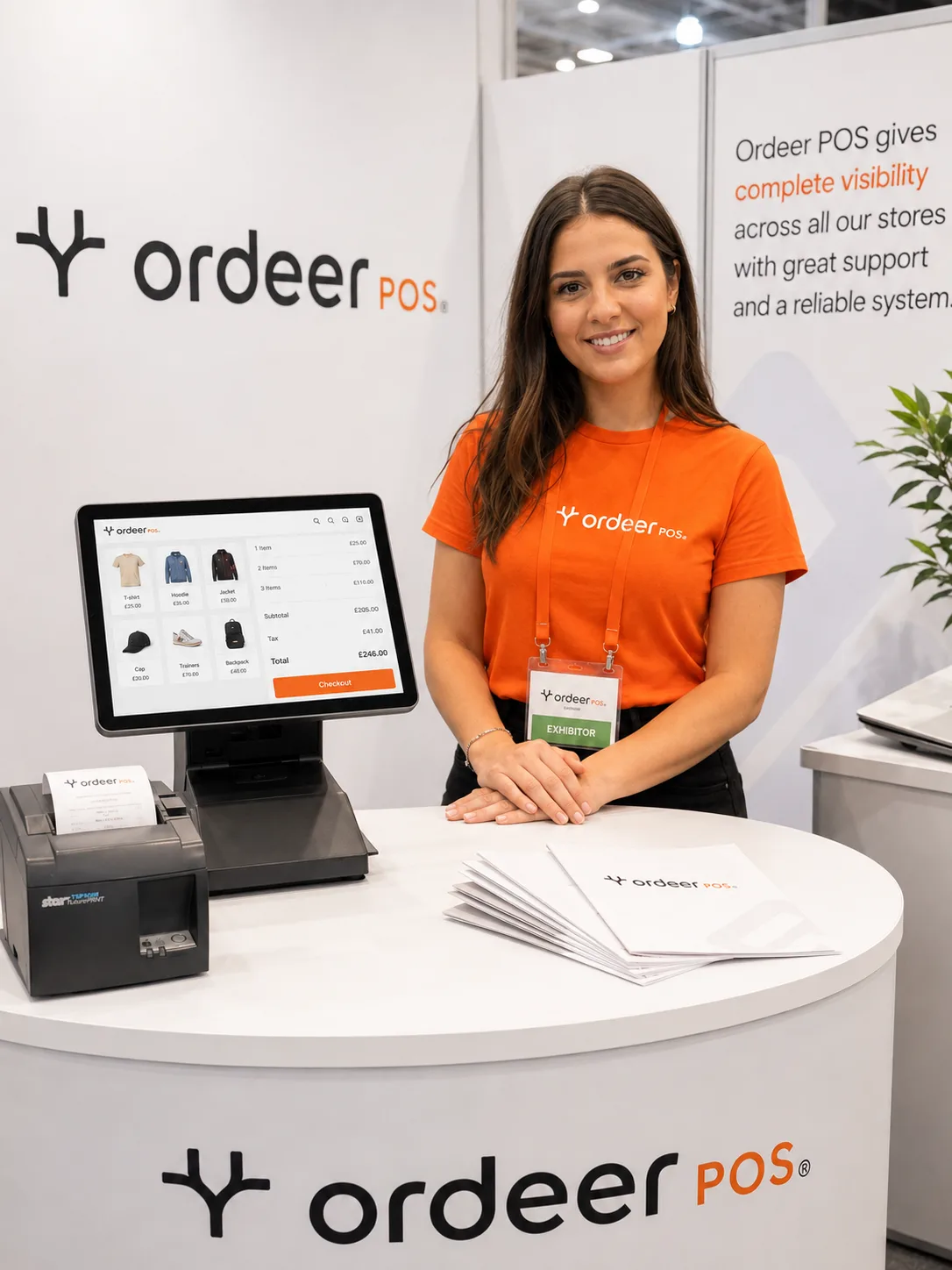 An Ordeer exhibition stand: a woman in an orange Ordeer shirt at the counter, beside an Ordeer EPOS till and receipt printer.
